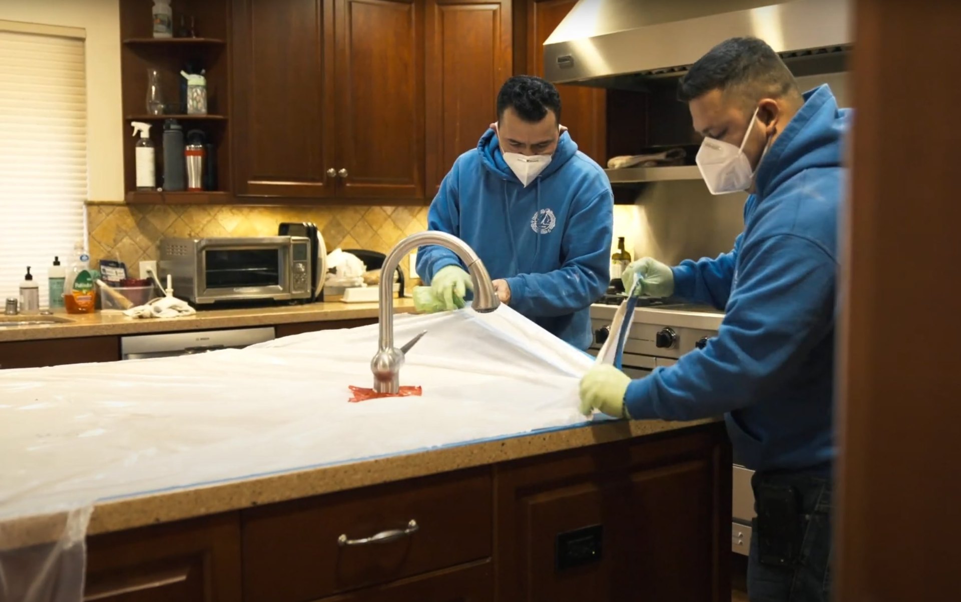 Professional water damage restoration technicians cleaning kitchen countertops and sink area with protective equipment