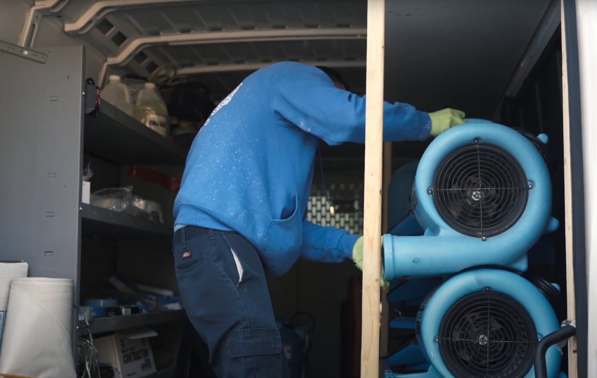 Professional water damage restoration technician in protective gear working with industrial drying equipment and blue air movers