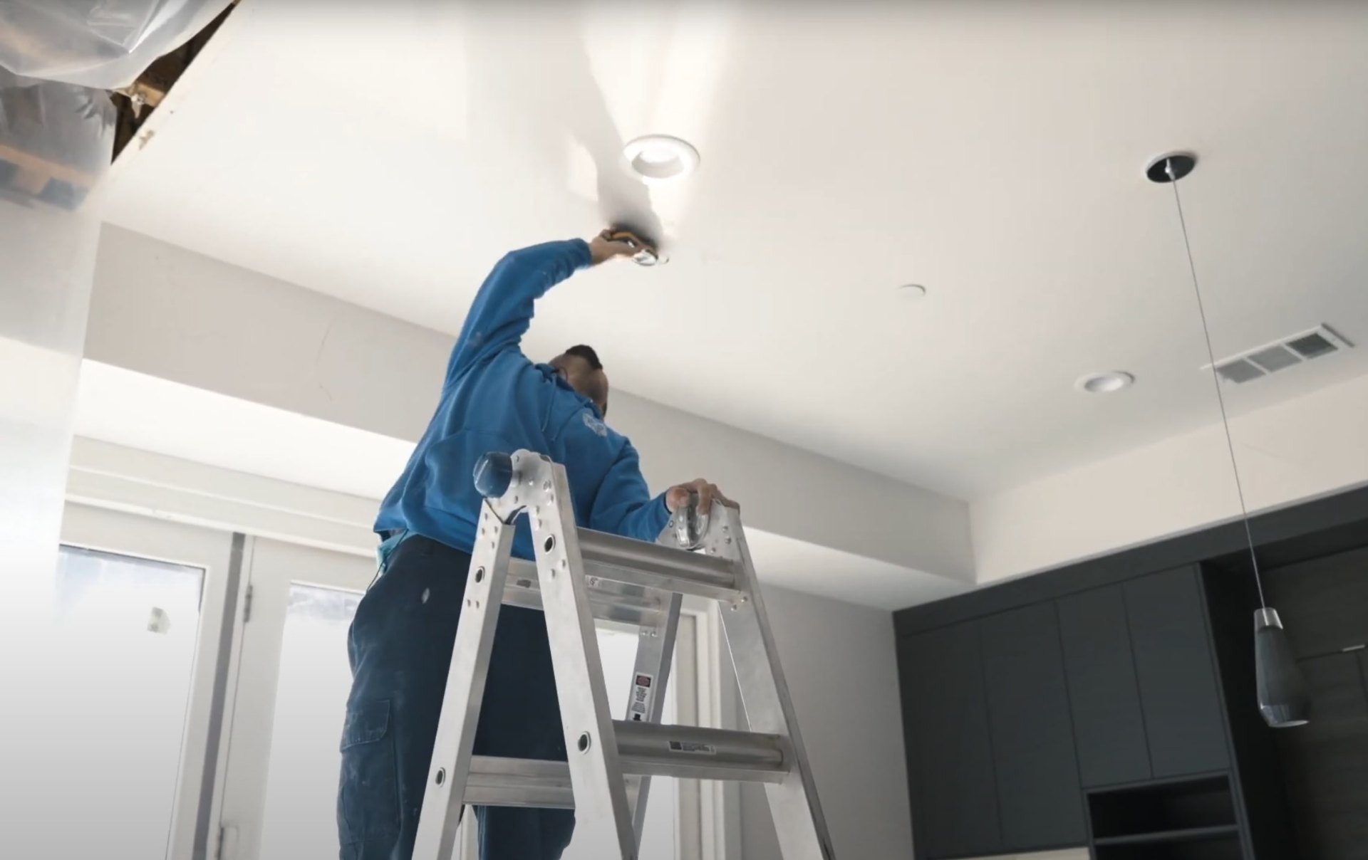 Water damage restoration specialist working on ceiling repair with professional ladder and equipment